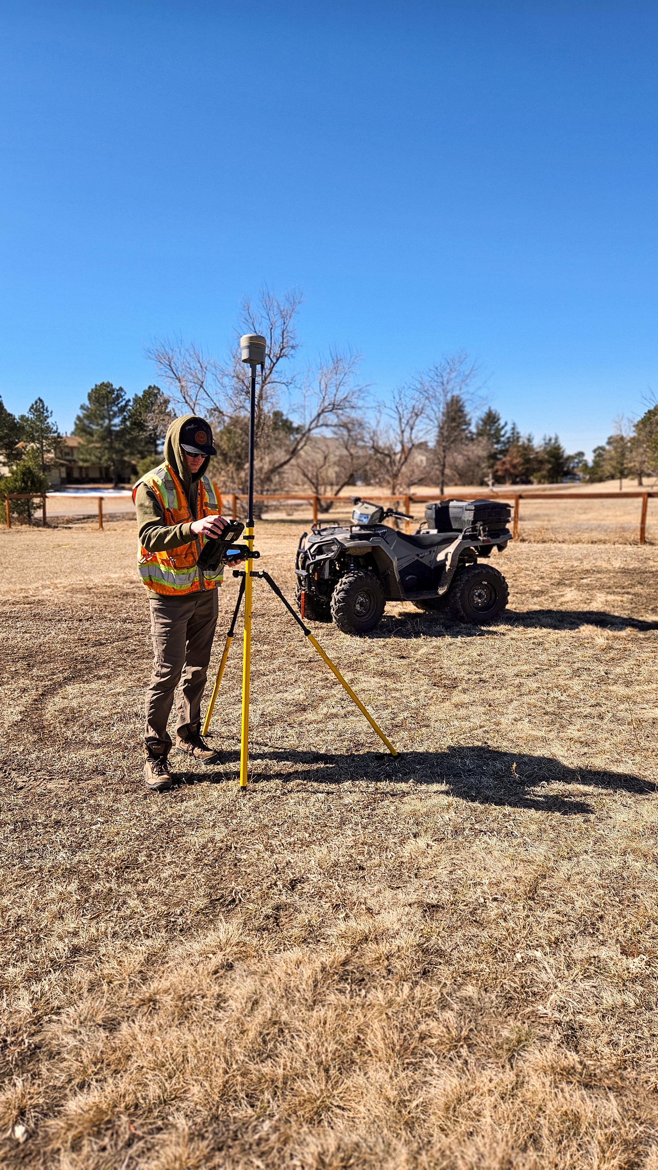 Person with surveying equipment in a field with an ATV in the background