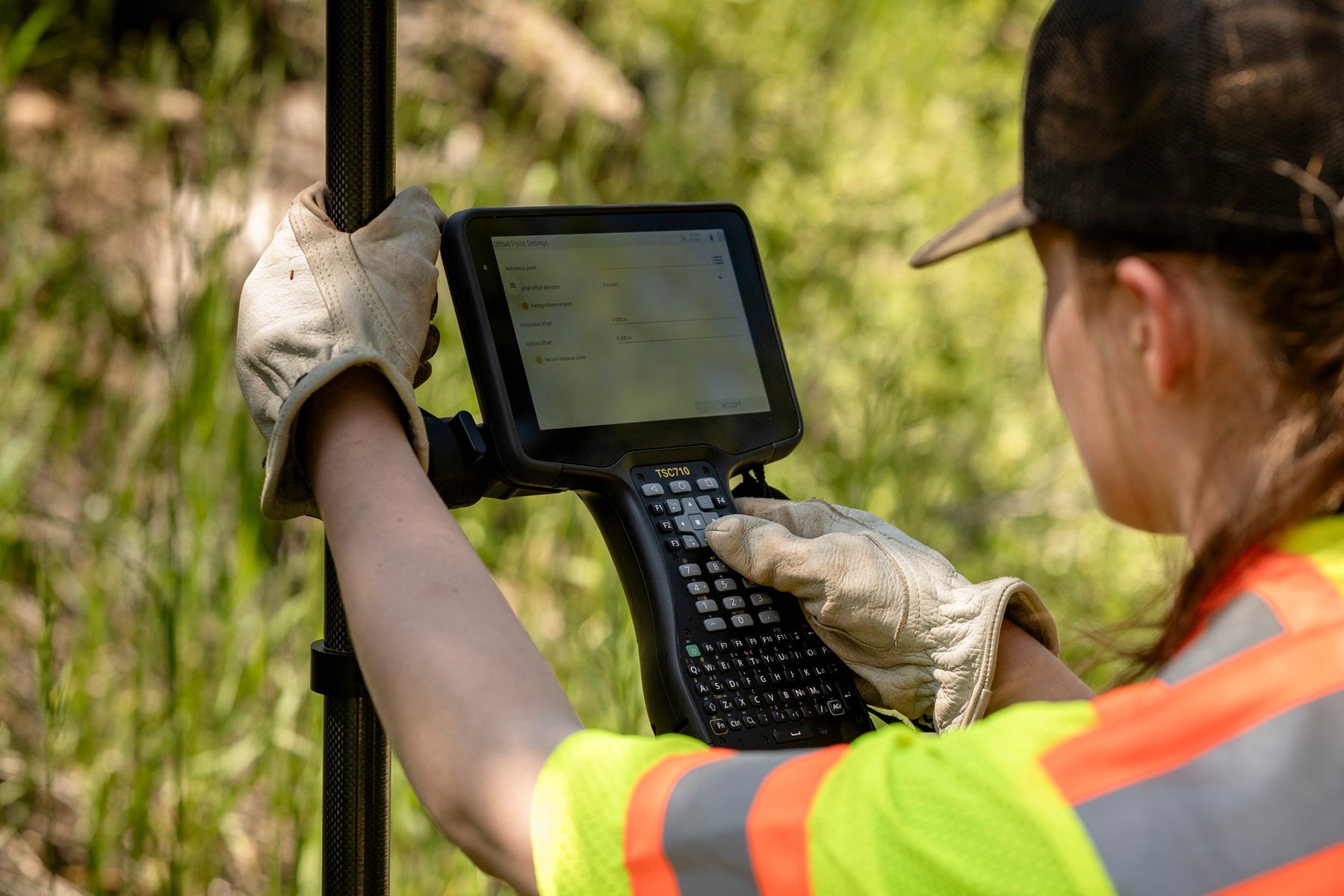 Surveyor in a forest using a TSC710 Data Collector, wearing a high-visibility vest.