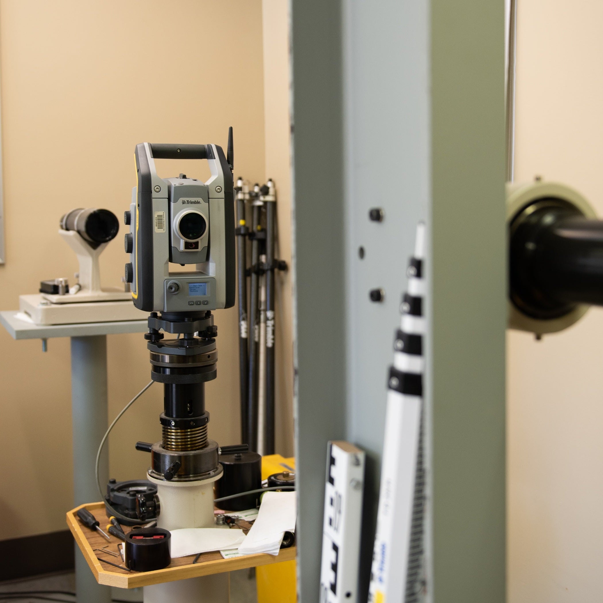 Measurement device on a stand against a wall with tools leaning against it.