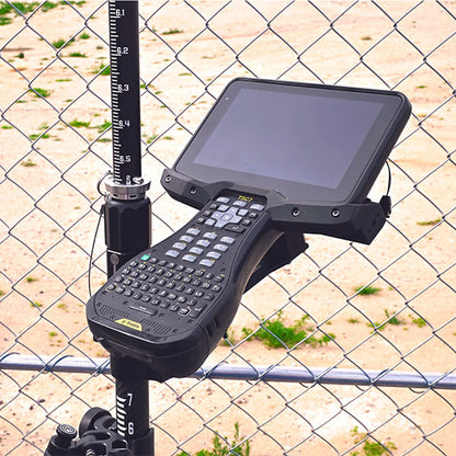 Trimble TSC7 mounted on a pole via bracket against a chain-link fence.