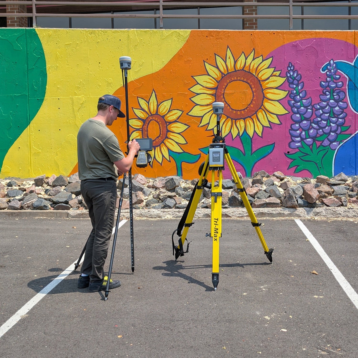 Person with surveying equipment in front of a colorful mural.