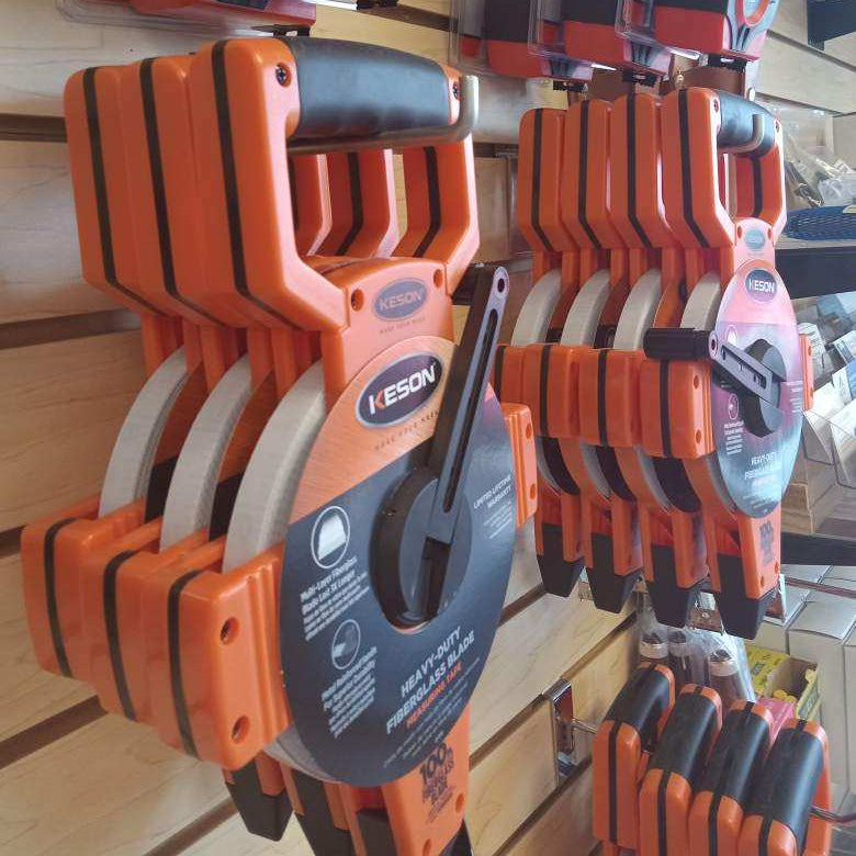 Set of orange Keson tape measures hanging on a display stand.