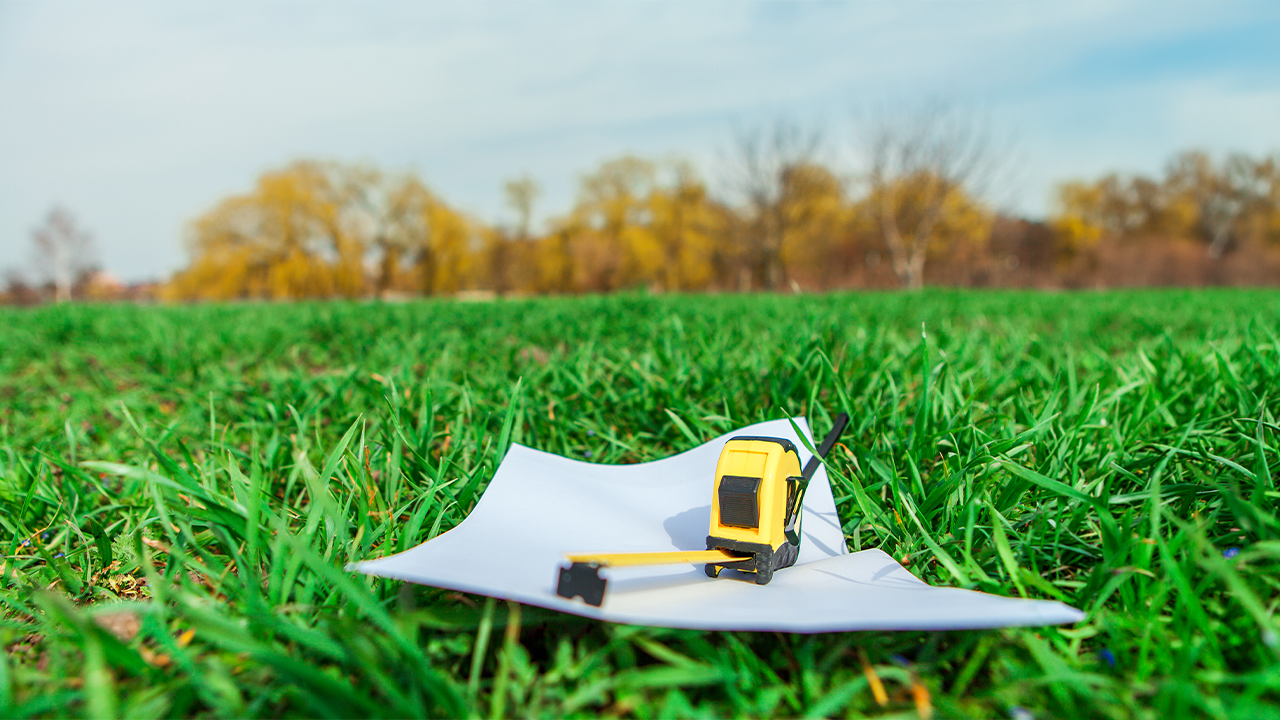 SECO pocket tape measure on a stack of paper in a grassy field. 